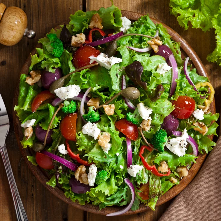 Ensalada verde con jitomate, queso y nuez servida en plato de madera